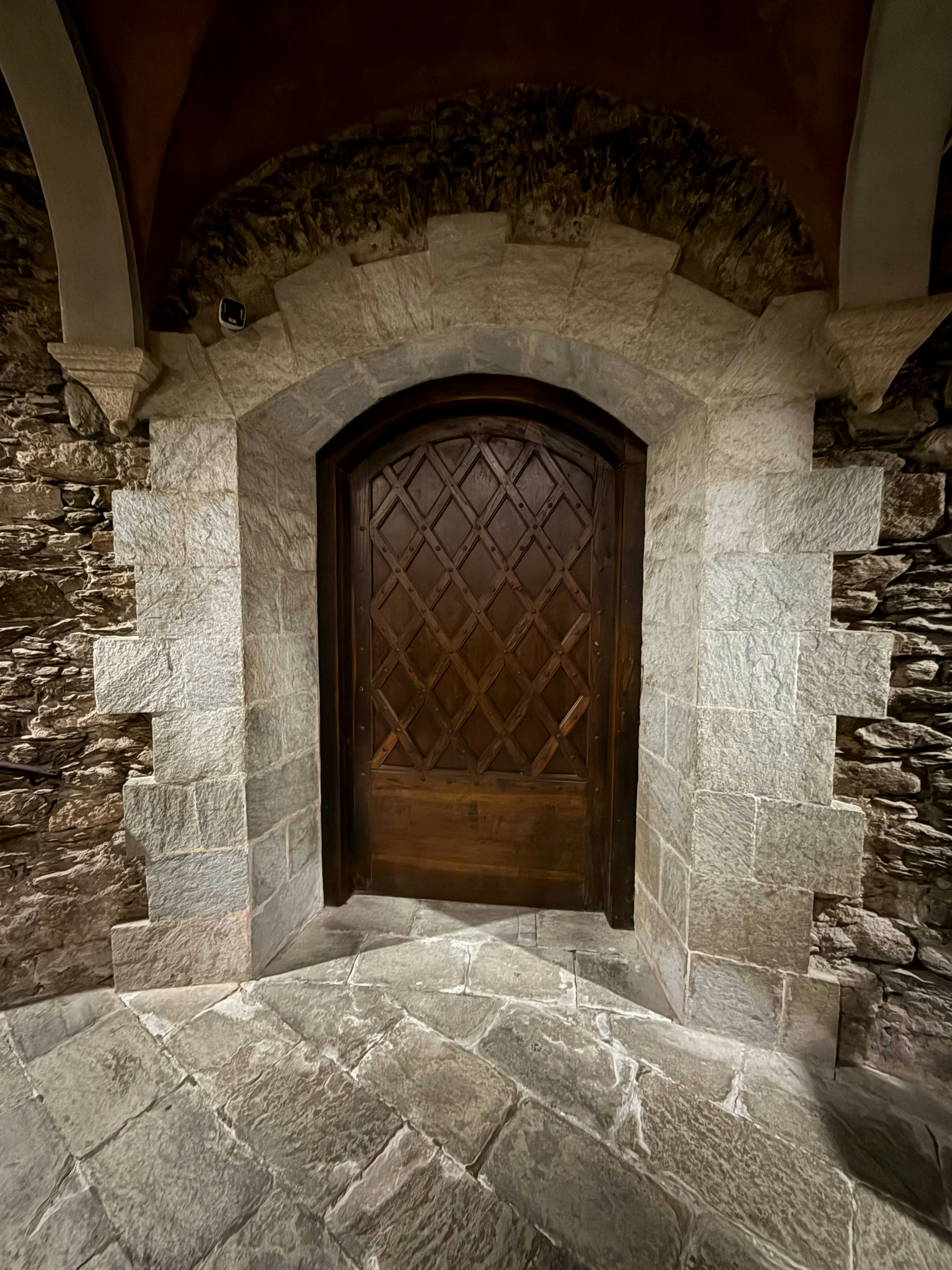 Arched custom wood door with diamond lattice carving set in a stone archway surround